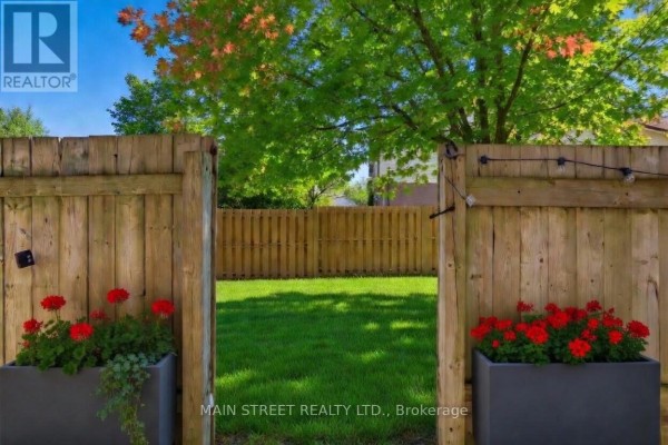 Backyard view through wooden gate with green grass, flower planters, string lights - 2 - 110 Silvan Drive Welland