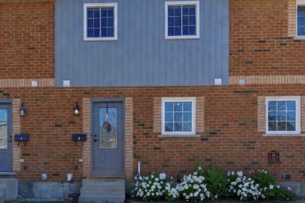 Renovated townhouse front with brick, blue siding, grid windows, flower beds - 2 - 110 Silvan Drive, Welland
