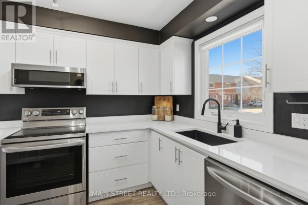 Modern kitchen with white cabinets, white counters, stainless steel appliances, black sink - 2 - 110 Silvan Drive, Welland