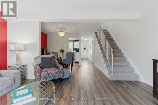 Open concept living room with wood-look floors, carpeted staircase, and dining area - 2 - 110 Silvan Drive, Welland