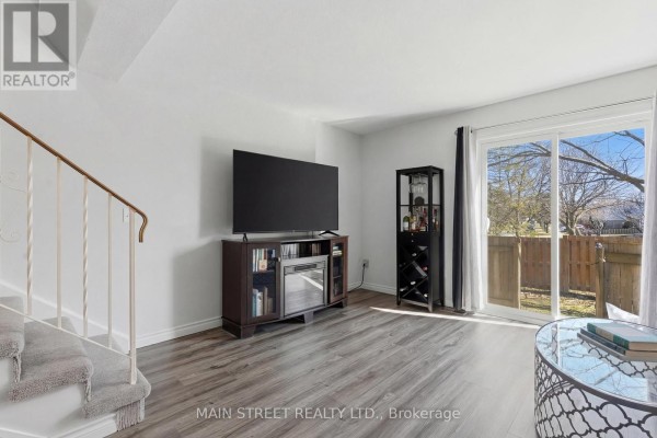 Living room with laminate floors, sliding glass door to fenced yard, and staircase - 2 - 110 Silvan Drive, Welland