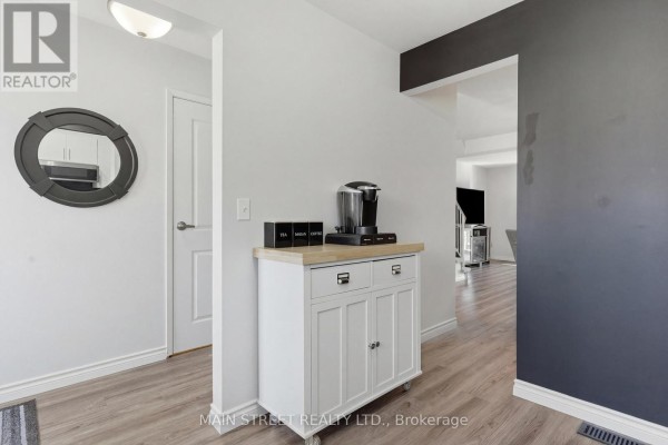 Hallway with light wood-look flooring, mobile cabinet, coffee maker, and round mirror - 2 - 110 Silvan Drive, Welland