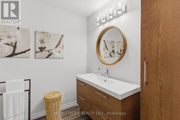 Modern bathroom with wood vanity, integrated sink, and round mirror - 2 - 110 Silvan Drive Welland