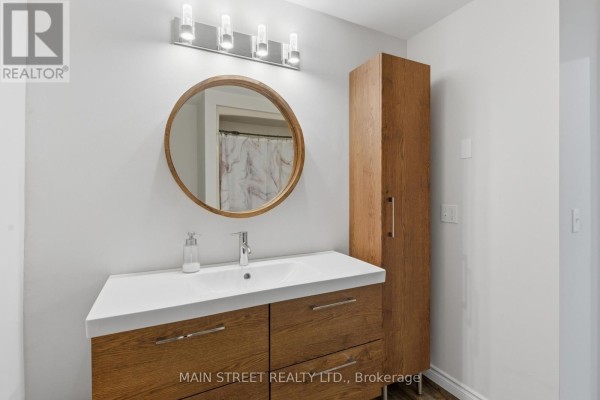 Renovated bathroom with wood vanity, round mirror, and storage cabinet - 2 - 110 Silvan Drive, Welland