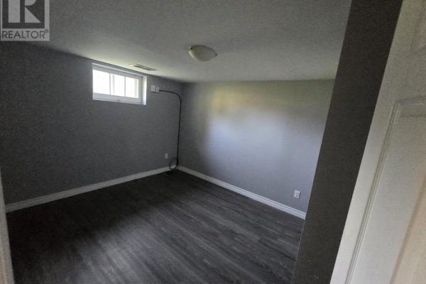 Empty grey room with a small window and dark wood-look flooring. - 2 - 113 Pitfield Road, Toronto