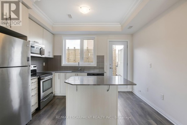 Kitchen area in a townhouse with stainless steel appliances, gray backsplash, and a central island. - 2 - 130 Frederick Tisdale Drive, Toronto