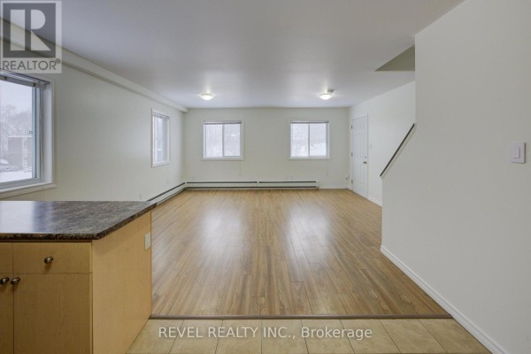 Living room with wood laminate flooring, white walls, and large windows. - 2 - 20 Puleston Street, Brantford