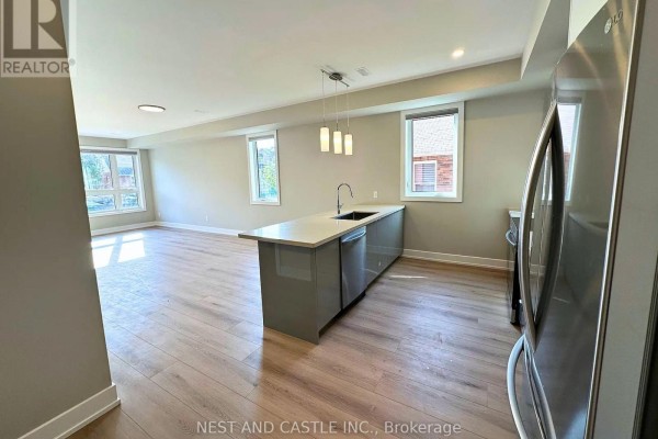 Open concept living area with grey floors, white walls, and a modern kitchen. - 2 - 20 West Street, Brampton