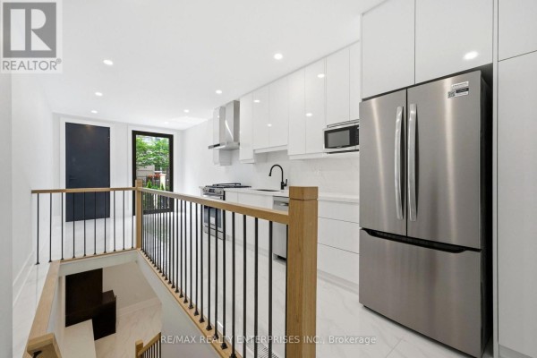 Kitchen view with stainless steel refrigerator, white cabinets, and a staircase with black railings. - 2 - 21 Belmont Street S, Toronto