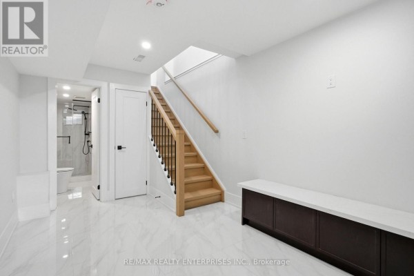 Basement hallway with a wooden staircase, built-in dark wood cabinets, and a door leading to a bathroom. - 2 - 21 Belmont Street S, Toronto