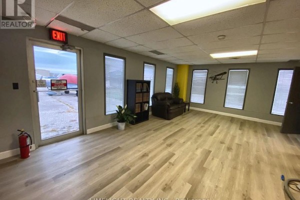 Interior reception area with grey walls, light wood floors, and a view of an airplane outside. - 2 - 2134 Crumlin Side Road, London East