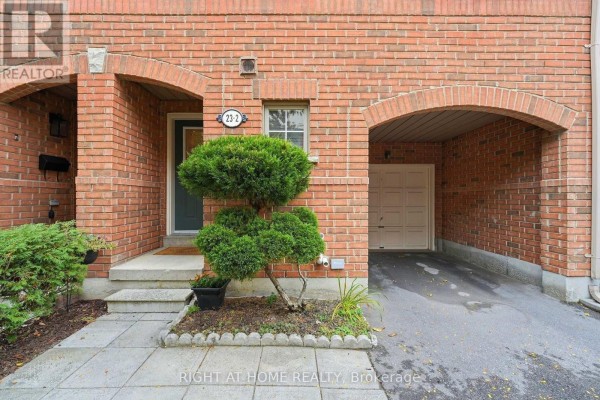 Front entrance of a townhouse with a covered walkway, garage, and manicured bushes. - 2 - 23 West Deane Park Drive, Toronto