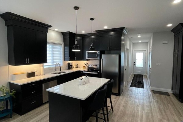 A modern kitchen with black cabinets, a white quartz island, stainless steel appliances, and light wood floors. - 2 - 255 Albert Street, Huron East