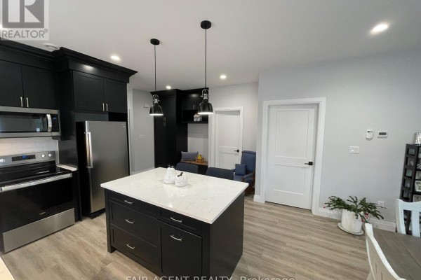 View of a kitchen island with chairs, dark cabinets, and a doorway to a seating area. - 2 - 255 Albert Street, Huron East