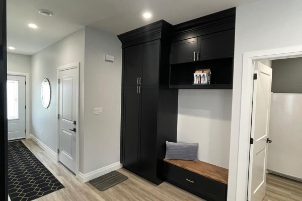 A hallway with light wood floors, white doors, and a black built-in cabinet with a wooden bench seat. - 2 - 255 Albert Street, Huron East