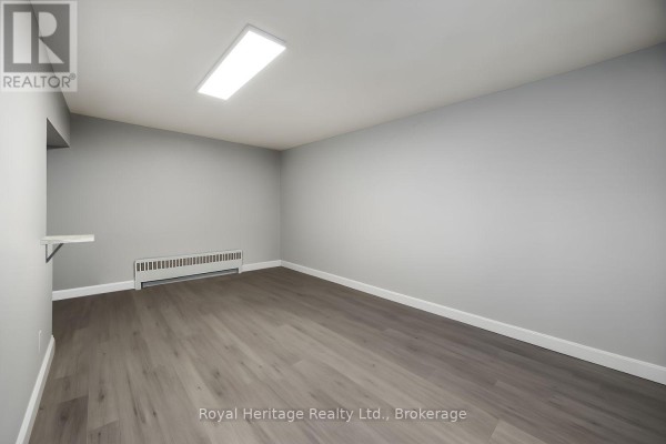Empty room with grey walls, laminate flooring, and a white ledge against the wall. - 2 - 264 Division Street, Cobourg