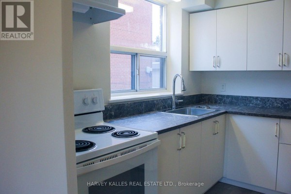 Corner view of the kitchen showing white cabinets, sink, faucet, and stove with window. - 2 - 28 Fraserwood Avenue, Toronto