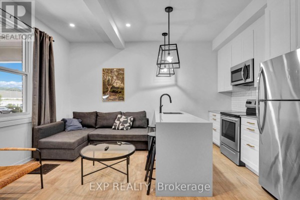 Living and kitchen area with grey sectional, white island, and large window with view. - 2 - 327 Catherine Street, Ottawa