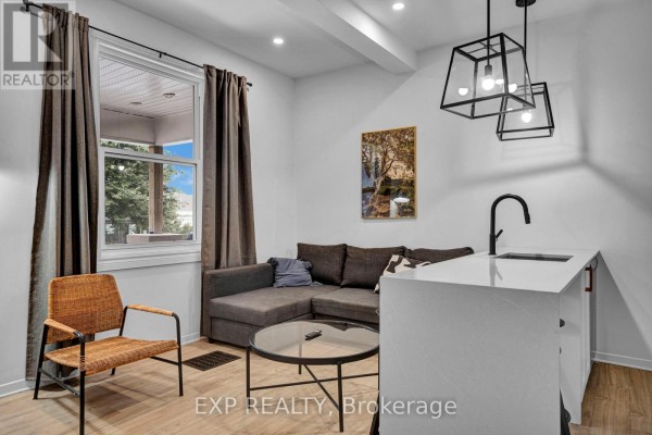 Living area featuring a grey sectional, wicker chair, coffee table, and window view. - 2 - 327 Catherine Street, Ottawa