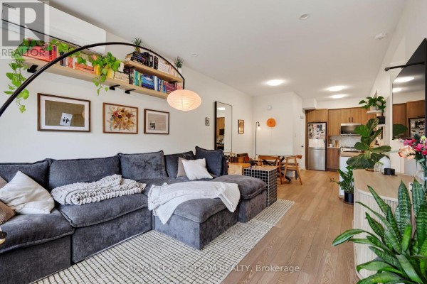 Living room with large sectional sofa, bookshelf, and open-concept kitchen area. - 2 - 353 Wilmont Avenue, Ottawa