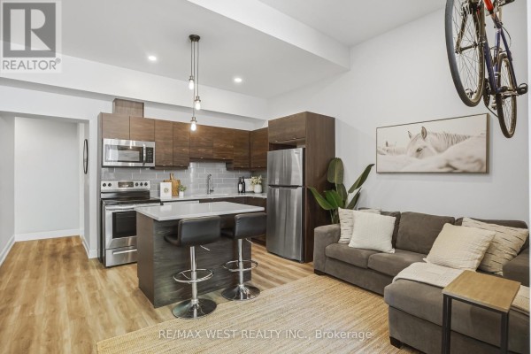 Open-concept living area with a kitchen island, sofa, and a bicycle on the wall. - 2 - 405 Merritt Street, St  Catharines