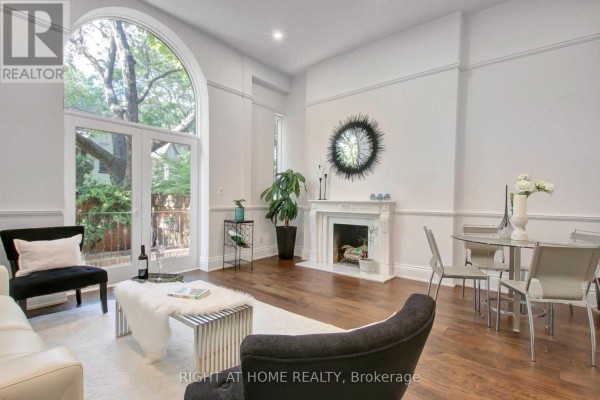 Living room with fireplace, arched glass doors, hardwood floors, and dining area. - 2 - 41 Spruce Street, Toronto