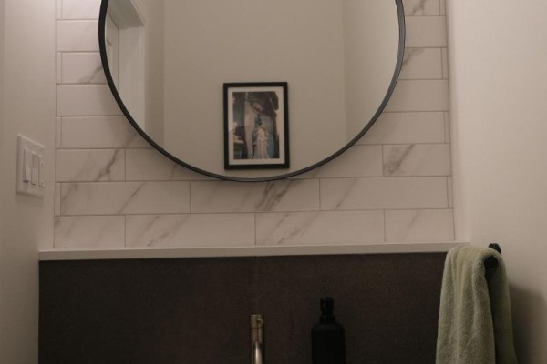 Powder room with marble tile backsplash, round mirror, and dark vanity. - 2 - 41 Spruce Street, Toronto