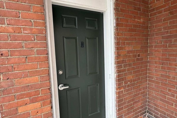 A dark green paneled door with a silver knob and a digital lock is set in a red brick wall. - 2 - 42 Toronto Street, Barrie