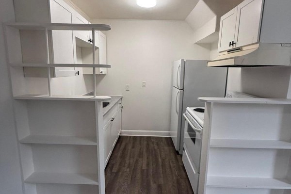 A galley kitchen with white cabinets, appliances, and open shelving units on either side. - 2 - 42 Toronto Street, Barrie