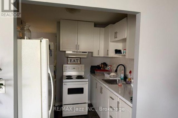 A small, galley-style kitchen with white cabinets, a white stove, and a stainless steel sink. - 2 - 43 Wayne Avenue, Oshawa