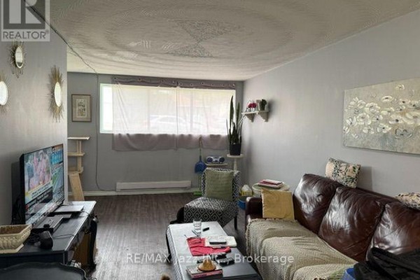 A living room with a brown leather sofa, a patterned armchair, and a television on a black stand. - 2 - 43 Wayne Avenue, Oshawa