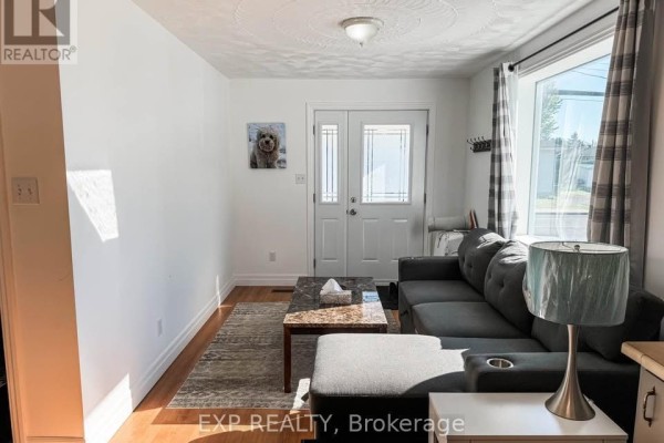 Living room with a gray sectional sofa, marble-top coffee table, and a large window with plaid curtains. - 2 - 4564 Ste Catherine Street, The Nation