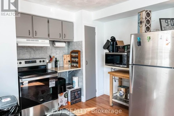 Kitchen view showing a stainless steel refrigerator, microwave, oven, and wooden flooring. - 2 - 4564 Ste Catherine Street, The Nation
