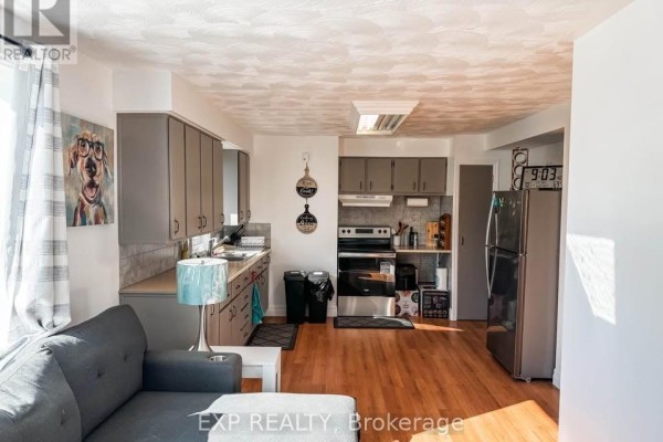 Open concept living room and kitchen area with gray cabinets, stainless steel appliances, and hardwood floors. - 2 - 4564 Ste Catherine Street, The Nation