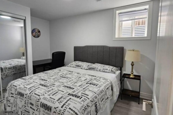Bedroom with a bed, desk, chair, nightstand, lamp, and mirrored closet door. - 2 - 54 Baycliffe Drive, Whitby