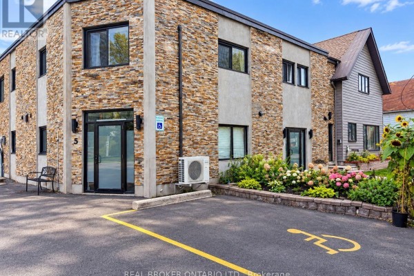 Exterior of multi-family building with stone and grey facade, accessible parking space. - 2 - 6610 Fourth Line Road, Ottawa