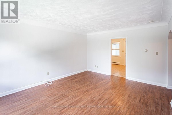 Living room with wood laminate flooring, white walls, and an arched doorway leading to a kitchen area. - 2 - 718 Ross Street, Burlington