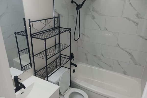 Bathroom with a white bathtub, marble-look tile walls, black fixtures, and a black metal shelving unit. - #2 10045 154 St Nw, Edmonton