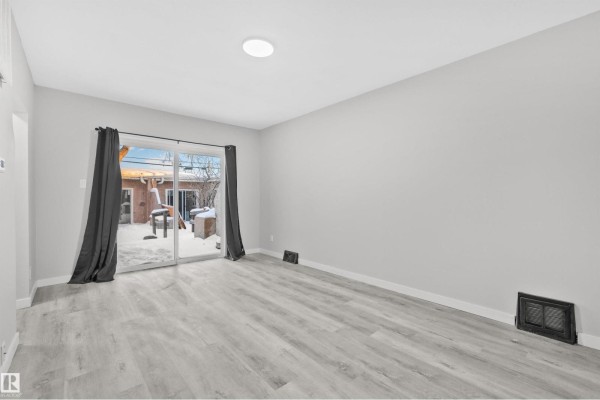 Living area with light gray walls, sliding glass doors leading to a snowy backyard, and light wood-look flooring. - #2 10049 154 St Nw, Edmonton