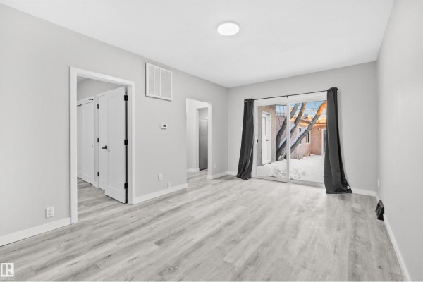 Living space with light gray walls, wood-look flooring, dark gray curtains, and doorways to other rooms. - #2 10049 154 St Nw, Edmonton