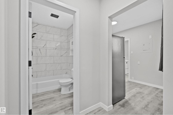 View into a bathroom with white tiled shower walls, toilet, and white bathtub, with light wood-look flooring. - #2 10049 154 St Nw, Edmonton