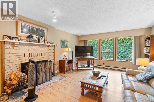 Living room with fireplace, hardwood floors, beige walls, and entryway door leading outside. - 2 1215 Stelly's Cross Rd, Central Saanich