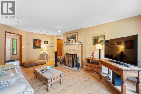 Living room with a white leather sofa, built-in bookshelf filled with books, and doorway to another room. - 2 1215 Stelly's Cross Rd, Central Saanich