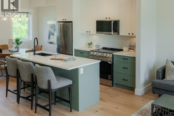 Open concept living and kitchen area with a green island, grey sofa, and light wood floors. - 2 1830 Allenby St, Saanich