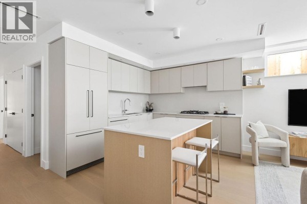 L-shaped kitchen with light wood island, white quartz countertops, and stainless steel appliances, adjacent to living space. - 2 2124 E 8 Avenue, Vancouver