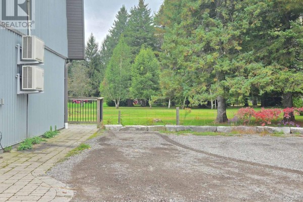 Gravel driveway and stone border with a fence and trees in the background. - 2-341 Queensville Side Road, East Gwillimbury