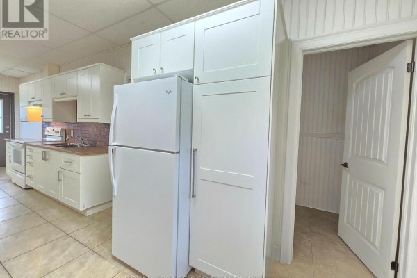 Kitchen with white cabinets, a refrigerator, and a pantry next to an open doorway. - 2-341 Queensville Side Road, East Gwillimbury