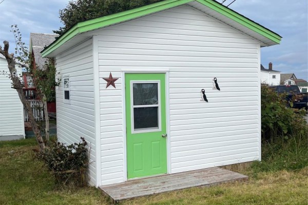 A small white shed with a green door and wooden steps sits on a grassy area. - 2-4 Russell's Lane, Bonavista