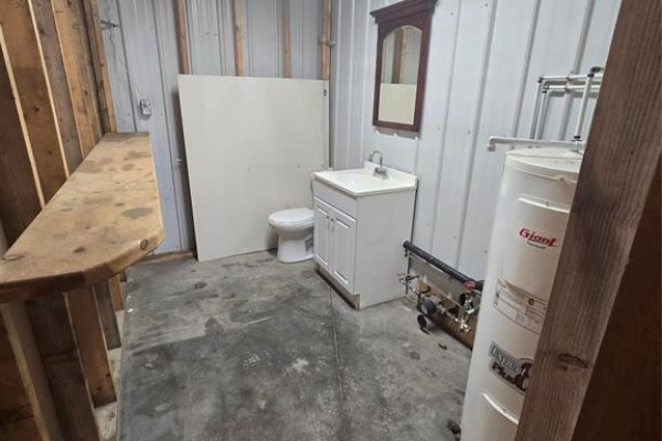 Small bathroom with white vanity, toilet, mirror, and large water heater in a commercial space. - 2 44 Industrial Road, Steinbach