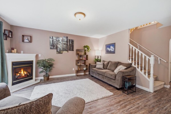 Living room featuring a fireplace, sofa, shelving unit, and stairs leading to the upper level of the townhouse. - 2 46360 Valleyview Road, Promontory, Chilliwack